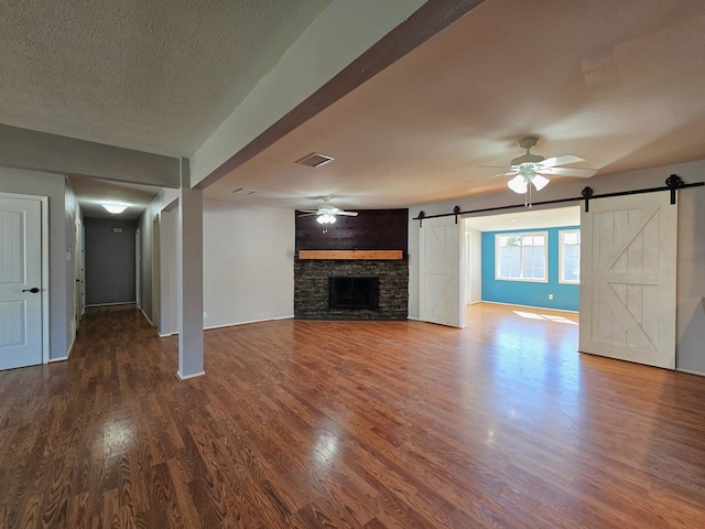 unfurnished living room with visible vents, a textured ceiling, wood finished floors, a barn door, and ceiling fan