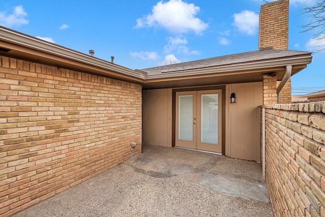 entrance to property with french doors, brick siding, a chimney, and a shingled roof