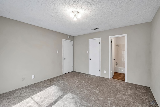 unfurnished bedroom featuring visible vents, carpet, ensuite bath, and a textured ceiling