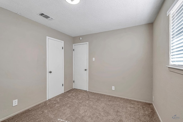 spare room featuring visible vents, a textured ceiling, baseboards, and carpet floors