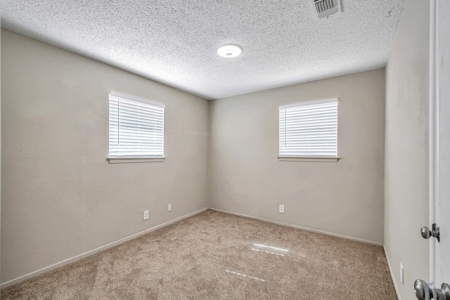 carpeted spare room featuring baseboards, visible vents, a wealth of natural light, and a textured ceiling