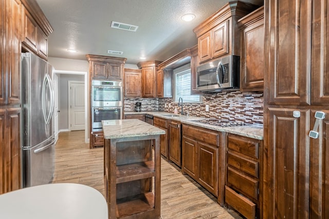 2205 Boyd Ave, Midland, TX 79705 - kitchen with stainless steel appliances, light wood-type flooring, backsplash, light stone counters, and a center island