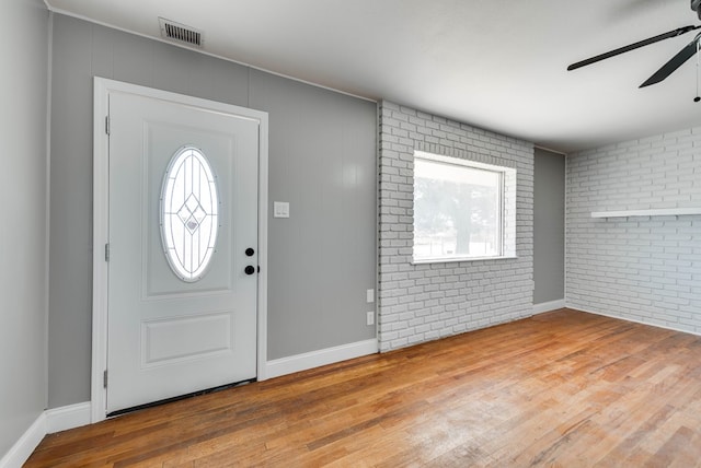 foyer entrance with brick wall, wood finished floors, visible vents, baseboards, and a ceiling fan