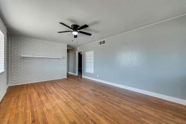 unfurnished room with brick wall, visible vents, and wood finished floors