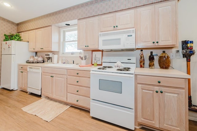 kitchen with white appliances, a sink, light countertops, light wood finished floors, and wallpapered walls