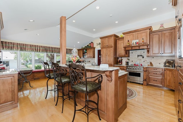 kitchen with lofted ceiling, brown cabinets, high end range, light stone countertops, and light wood-style floors