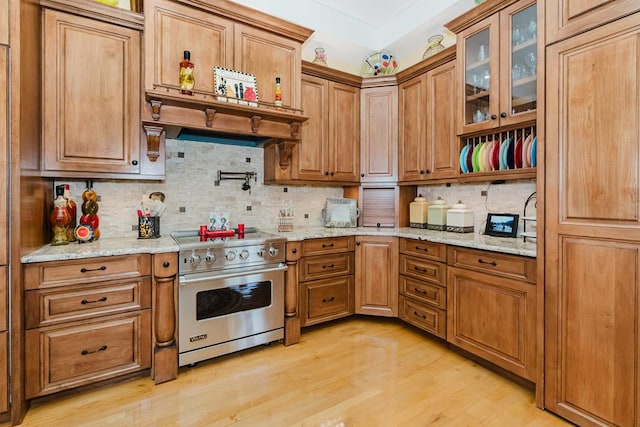 kitchen with light wood-type flooring, tasteful backsplash, brown cabinets, and stainless steel stove