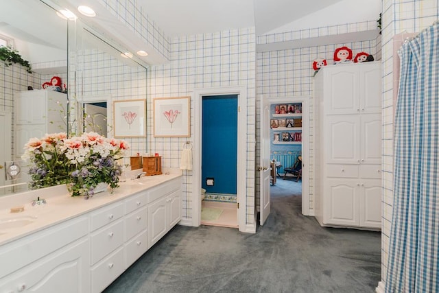 full bath with double vanity, a sink, and tile walls