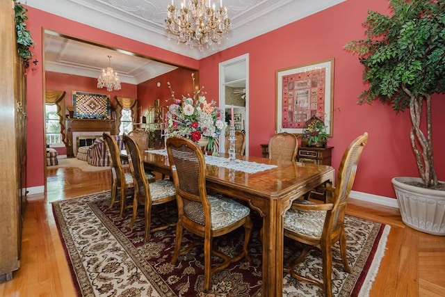 dining space with baseboards, ornamental molding, wood finished floors, a fireplace, and a notable chandelier