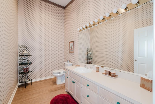 bathroom featuring wood finished floors, vanity, baseboards, ornamental molding, and wallpapered walls