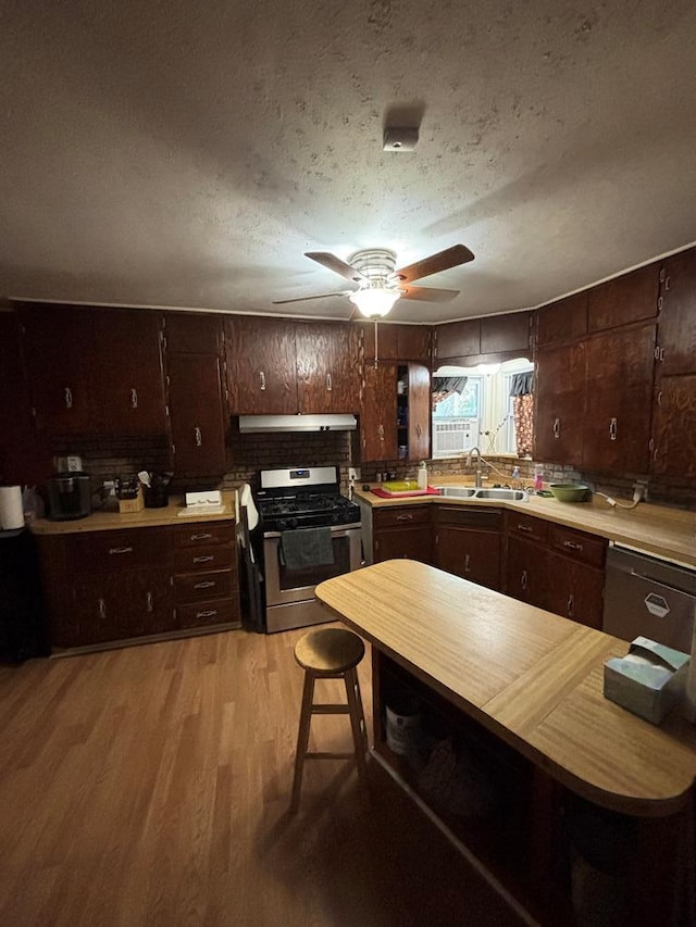 3103 Hill Ave, Snyder, TX 79549 - kitchen with stainless steel gas range oven, a sink, under cabinet range hood, light wood-style floors, and a textured ceiling