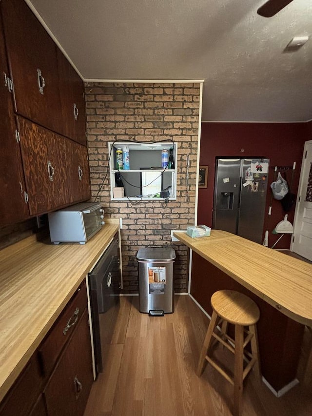 3103 Hill Ave, Snyder, TX 79549 - kitchen featuring stainless steel refrigerator with ice dispenser, butcher block counters, wood finished floors, brick wall, and dark brown cabinetry