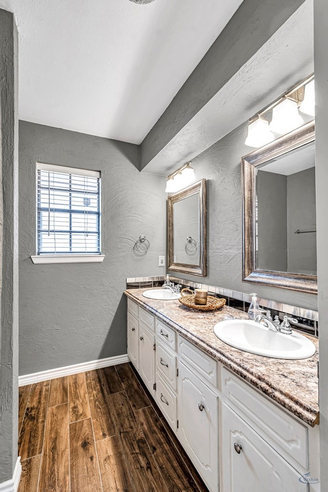 bathroom featuring a sink, a textured wall, double vanity, and wood finished floors