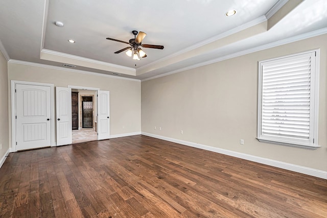 empty room with crown molding, ceiling fan, a tray ceiling, and dark hardwood / wood-style flooring