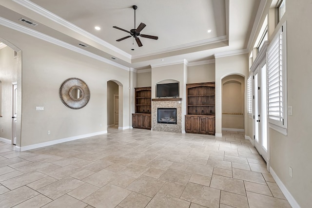 unfurnished living room featuring a raised ceiling, crown molding, ceiling fan, and built in shelves