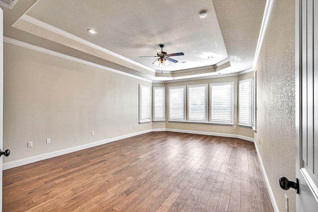 empty room with ornamental molding, a raised ceiling, hardwood / wood-style floors, and a textured ceiling