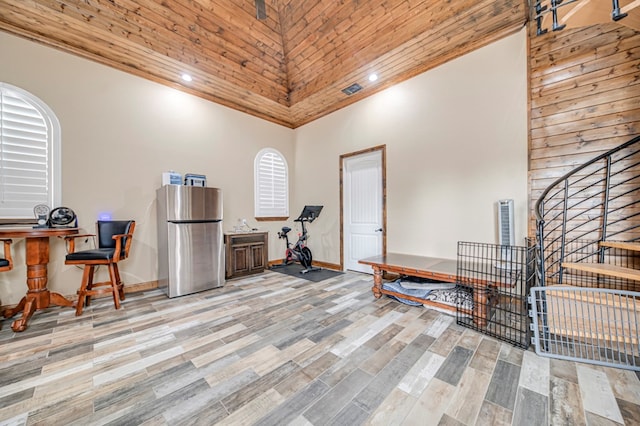 exercise area featuring a towering ceiling, light hardwood / wood-style floors, and wood ceiling