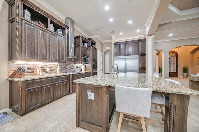 kitchen featuring built in appliances, light stone counters, sink, and a kitchen island with sink