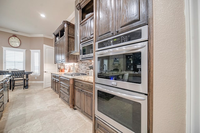 kitchen with dark brown cabinetry, light stone countertops, tasteful backsplash, crown molding, and appliances with stainless steel finishes