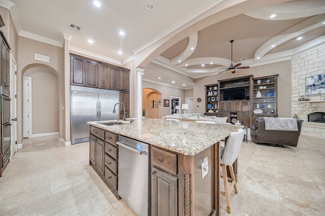 kitchen featuring ceiling fan, light stone countertops, a fireplace, an island with sink, and stainless steel appliances