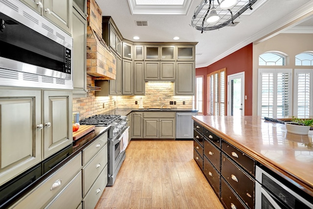 kitchen with appliances with stainless steel finishes, a sink, crown molding, light wood-type flooring, and backsplash