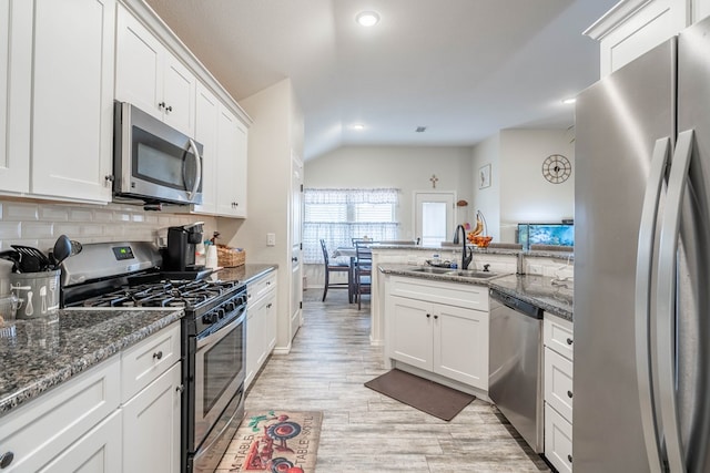 kitchen featuring appliances with stainless steel finishes, sink, white cabinets, dark stone counters, and light hardwood / wood-style flooring