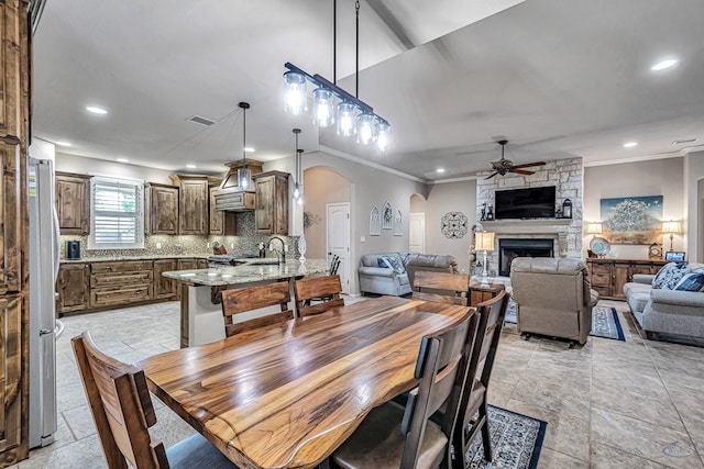 dining room with arched walkways, a stone fireplace, stone tile floors, visible vents, and a ceiling fan
