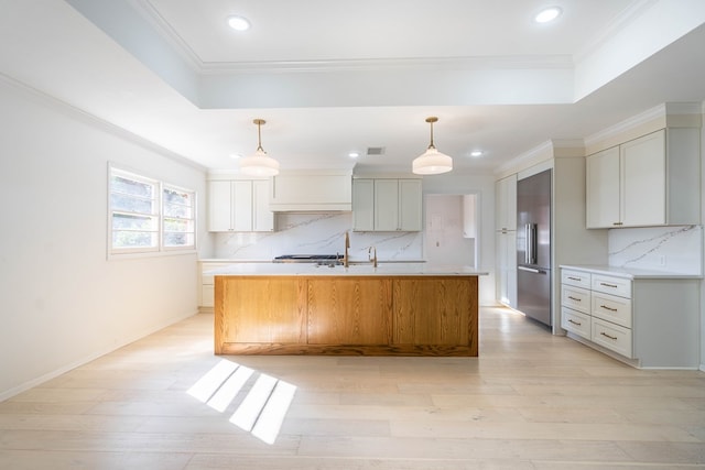 kitchen with backsplash, an island with sink, decorative light fixtures, and built in refrigerator