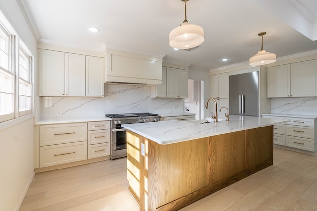 kitchen with light stone counters, an island with sink, backsplash, high quality appliances, and pendant lighting