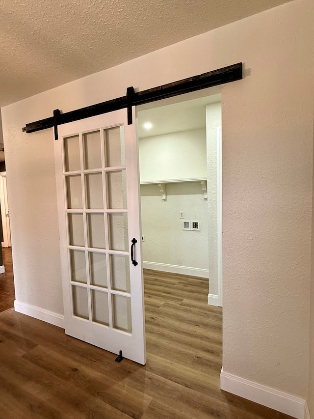 hallway featuring baseboards, wood finished floors, a barn door, a textured wall, and a textured ceiling