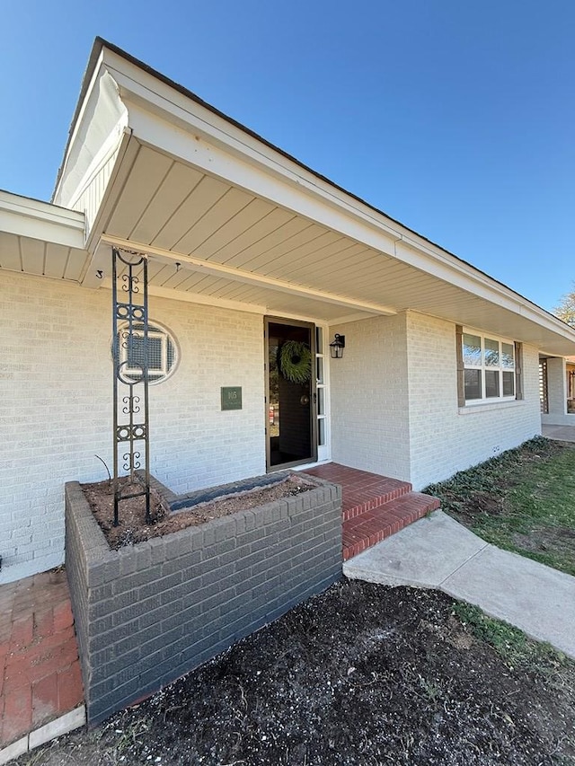 doorway to property featuring brick siding and a porch
