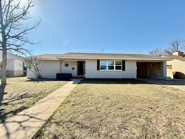 ranch-style home featuring brick siding, an attached carport, a front lawn, and roof with shingles