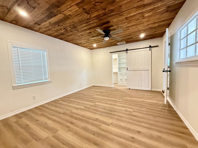 unfurnished bedroom featuring wood ceiling, a spacious closet, light wood-type flooring, ceiling fan, and a barn door