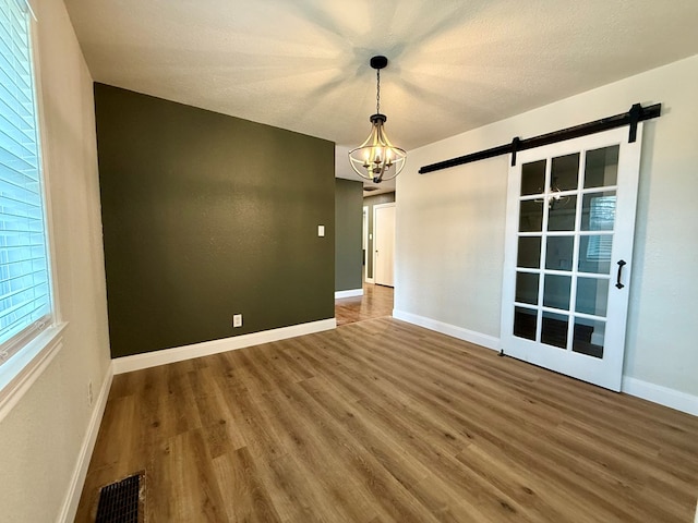 spare room featuring hardwood / wood-style floors, a textured ceiling, a barn door, and a chandelier