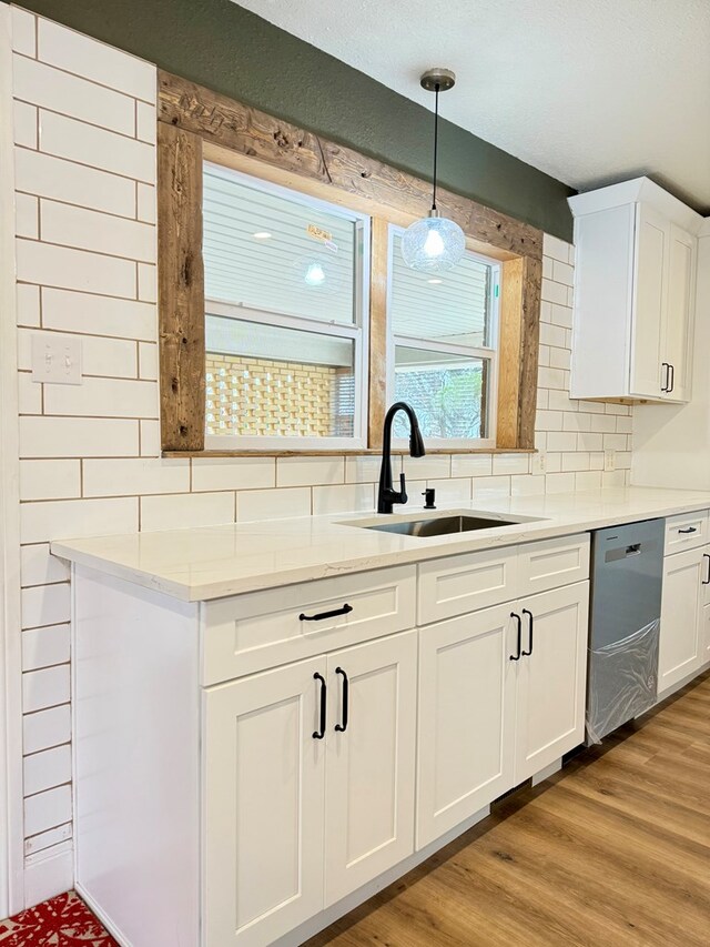kitchen featuring white cabinetry, light wood-style flooring, a sink, decorative backsplash, and stainless steel dishwasher