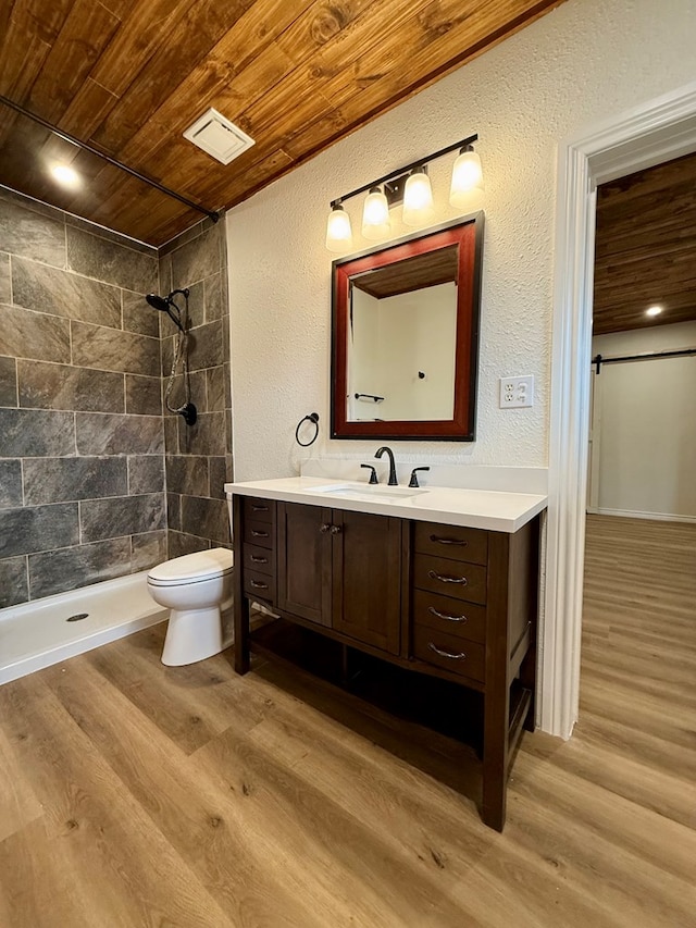 bathroom featuring tiled shower, toilet, wood-type flooring, wooden ceiling, and vanity