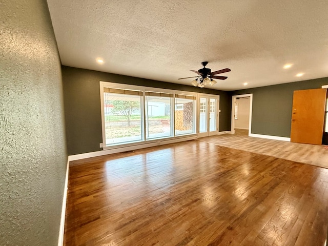 unfurnished living room with visible vents, baseboards, wood finished floors, a textured wall, and a ceiling fan