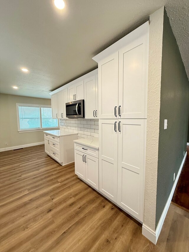 kitchen with white cabinetry, wood-type flooring, and decorative backsplash