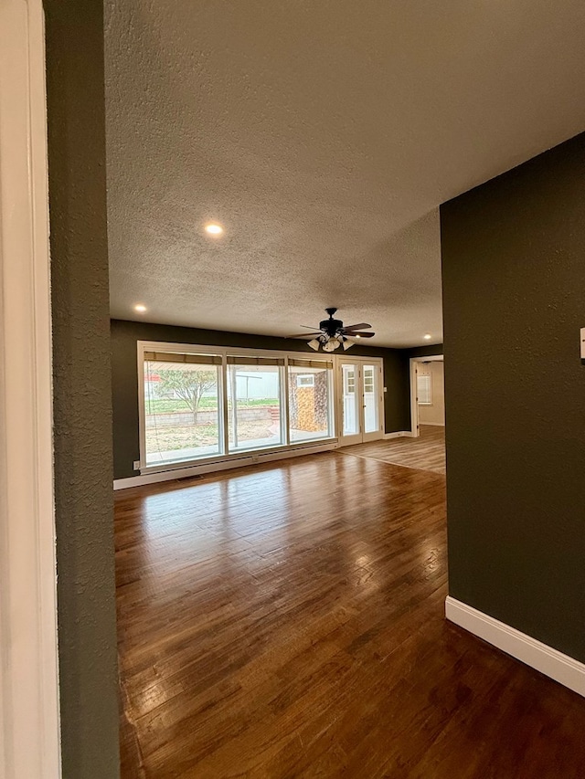 empty room with a ceiling fan, a textured ceiling, wood finished floors, baseboards, and a textured wall