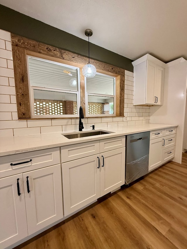 kitchen with white cabinetry, a sink, light wood-style floors, stainless steel dishwasher, and tasteful backsplash