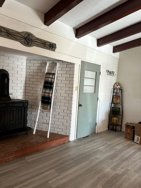 unfurnished living room featuring wood-type flooring, beamed ceiling, and a wood stove