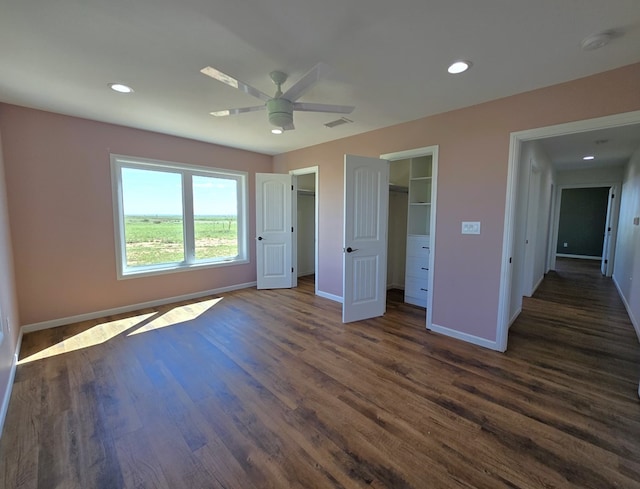 unfurnished bedroom featuring ceiling fan, dark hardwood / wood-style floors, a closet, and a walk in closet