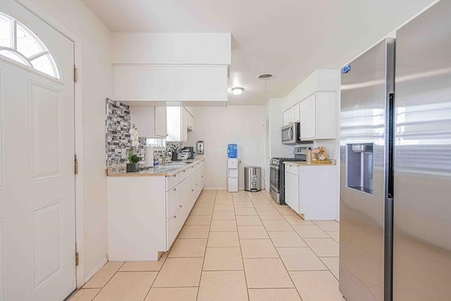 kitchen featuring appliances with stainless steel finishes, backsplash, sink, light tile patterned floors, and white cabinetry