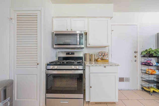 kitchen with light stone counters, stainless steel appliances, white cabinetry, and light tile patterned flooring