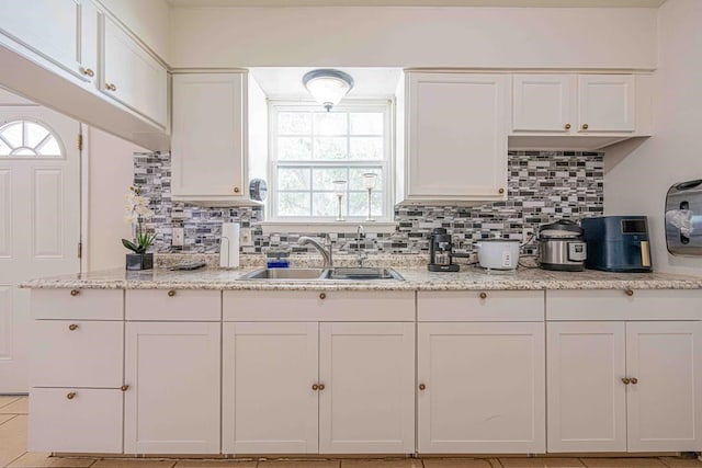 kitchen featuring light stone countertops, backsplash, sink, light tile patterned floors, and white cabinetry