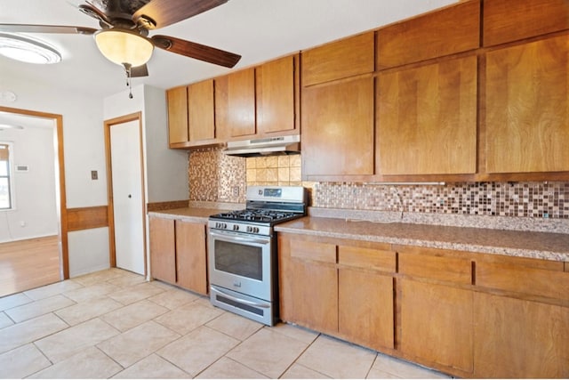 kitchen featuring decorative backsplash, stainless steel gas range oven, light tile patterned floors, and ceiling fan