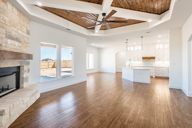 unfurnished living room with baseboards, arched walkways, wood ceiling, dark wood-type flooring, and a stone fireplace