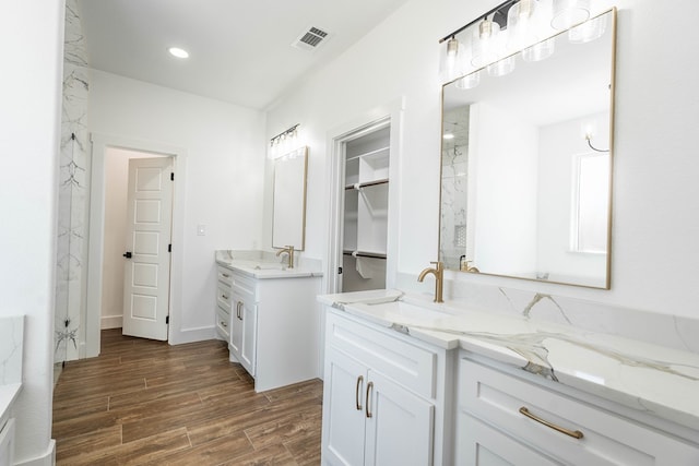 full bathroom featuring two vanities, wood finished floors, a walk in closet, a sink, and recessed lighting