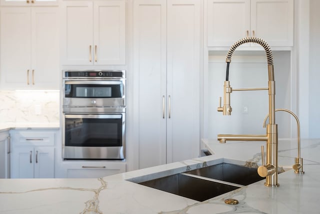 kitchen featuring stainless steel double oven, white cabinets, decorative backsplash, and light stone countertops