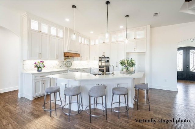 kitchen with an island with sink, arched walkways, light countertops, and white cabinets